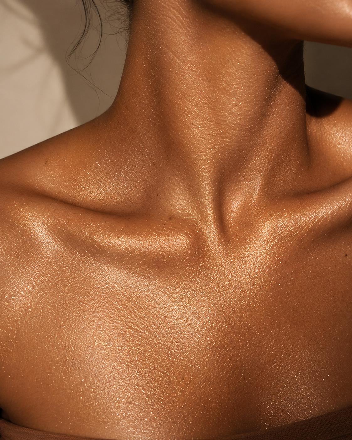 Close-up of a person's neck and upper chest with glossy, warm bronze-toned skin and subtle shimmer.